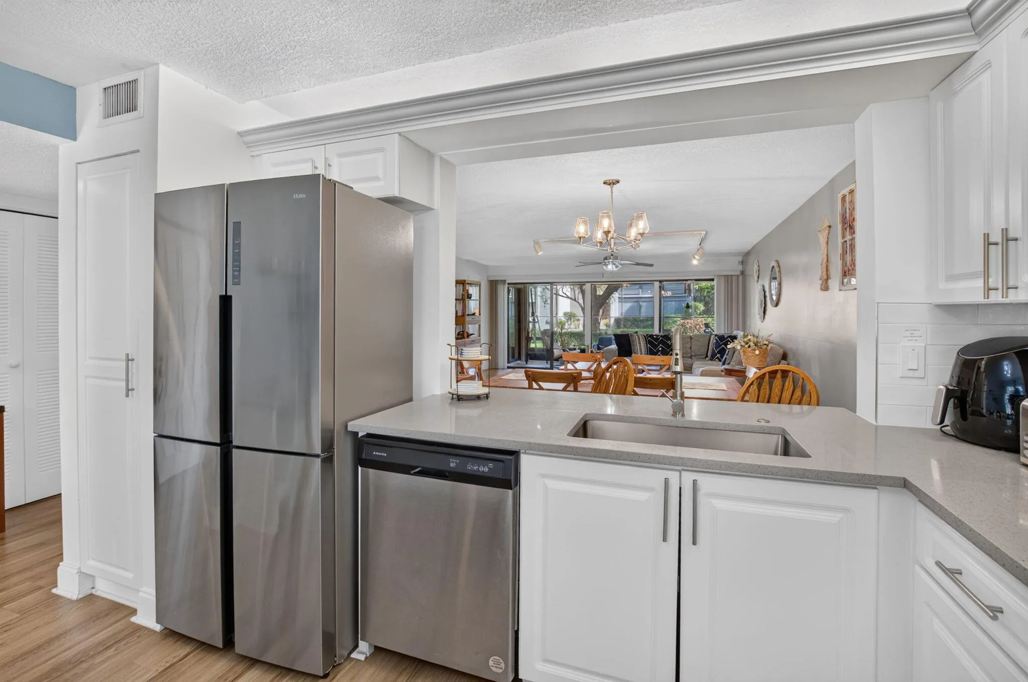 White shaker-style cabinetry, stainless steel appliances, quartz countertops, subway tile backsplash, and wood-finish flooring