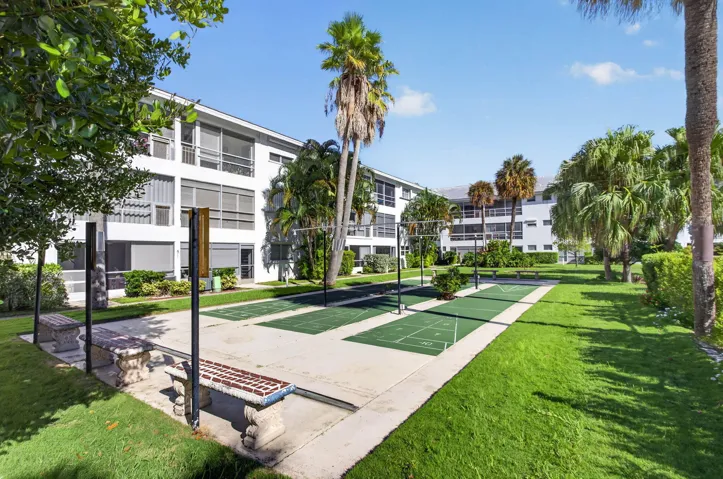 Expansive green space featuring shuffleboard courts, concrete benches, and mature palm trees
