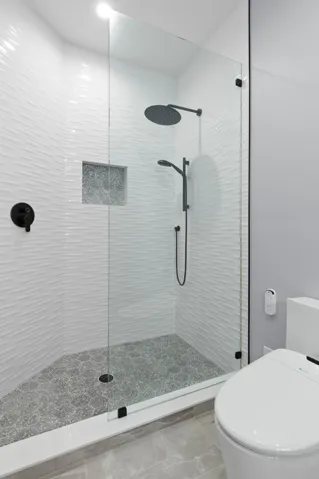 The ensuite continues with a glass-enclosed walk-in shower, rainfall and handheld showerheads, and striking textured tile for a crisp, contemporary finish.