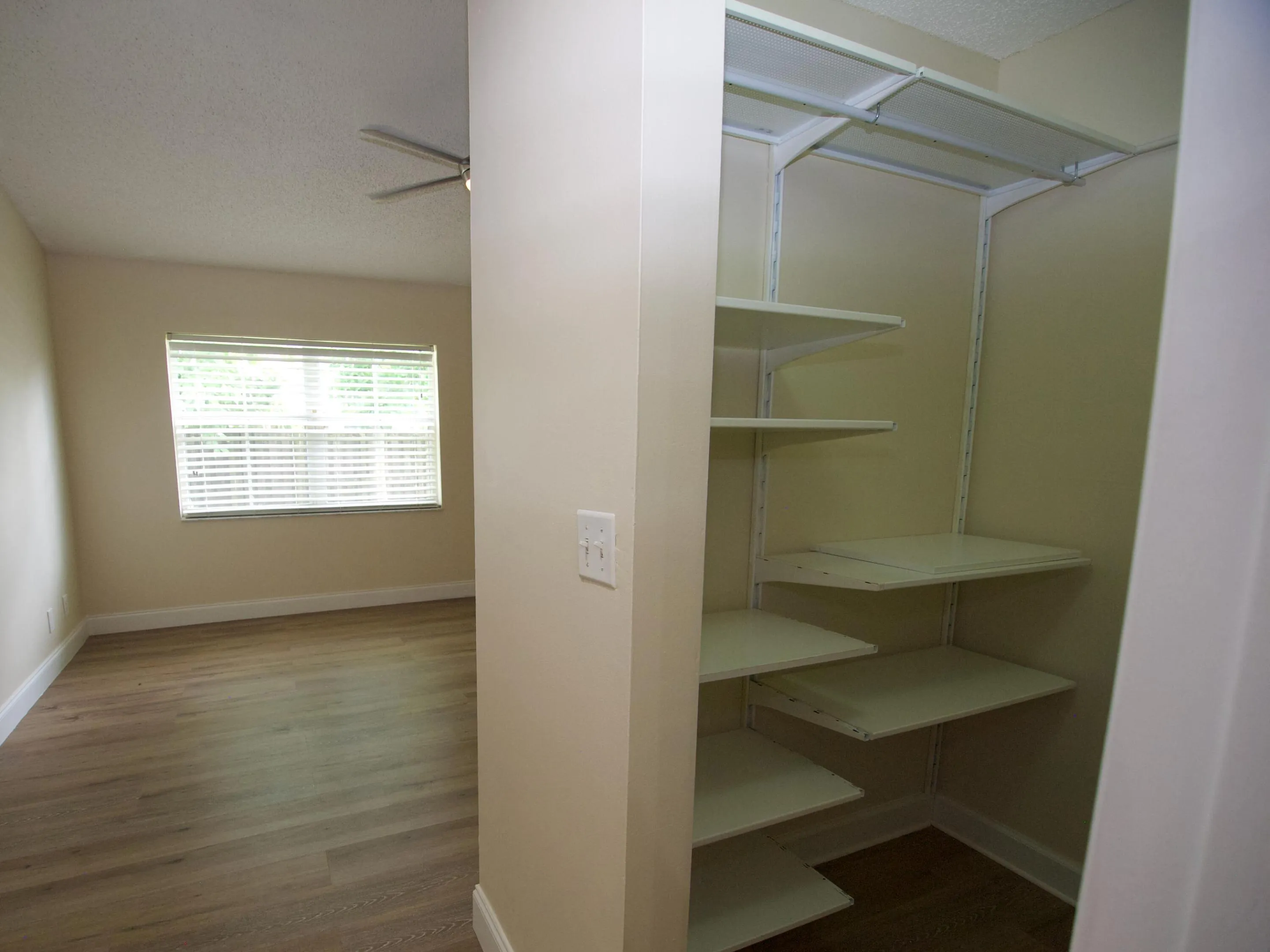 Neutral wall color, wood-finish flooring, ceiling fan, window with blinds, and built-in closet shelving