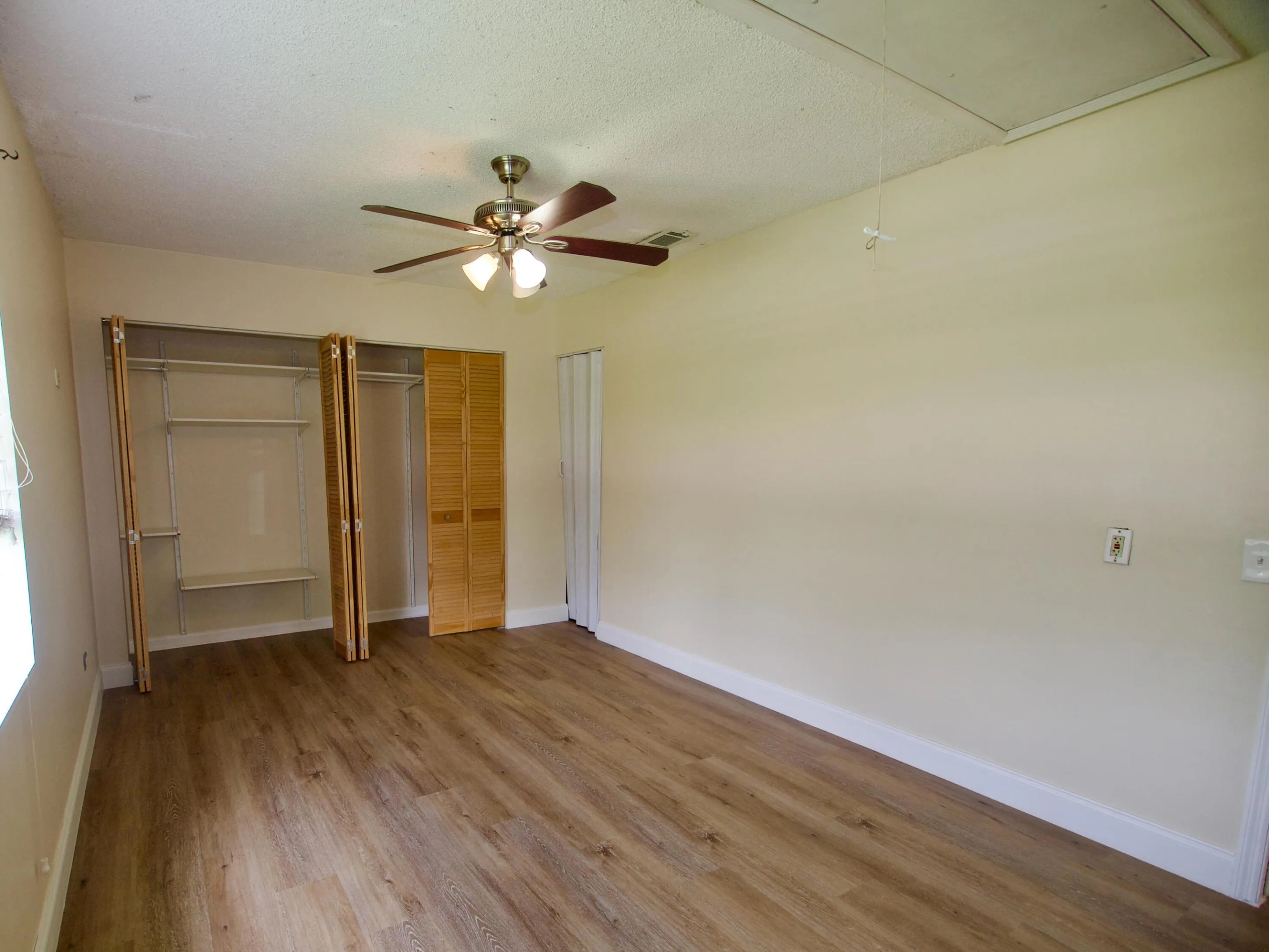 Wood-finish flooring, bi-fold closet doors, built-in closet shelving, and a ceiling fan with integrated lighting