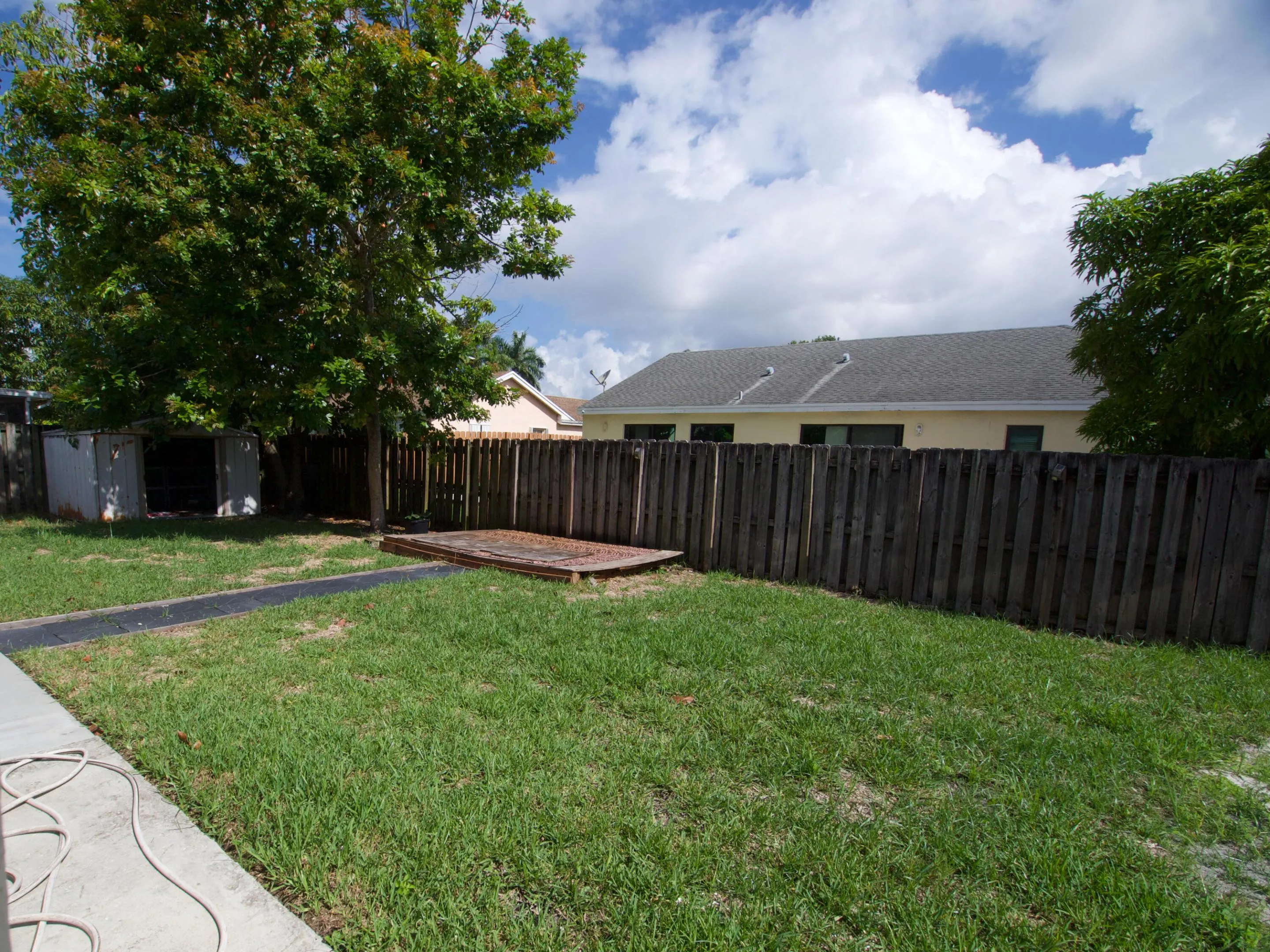 Expansive green lawn with a wooden privacy fence, mature trees, and a concrete patio area