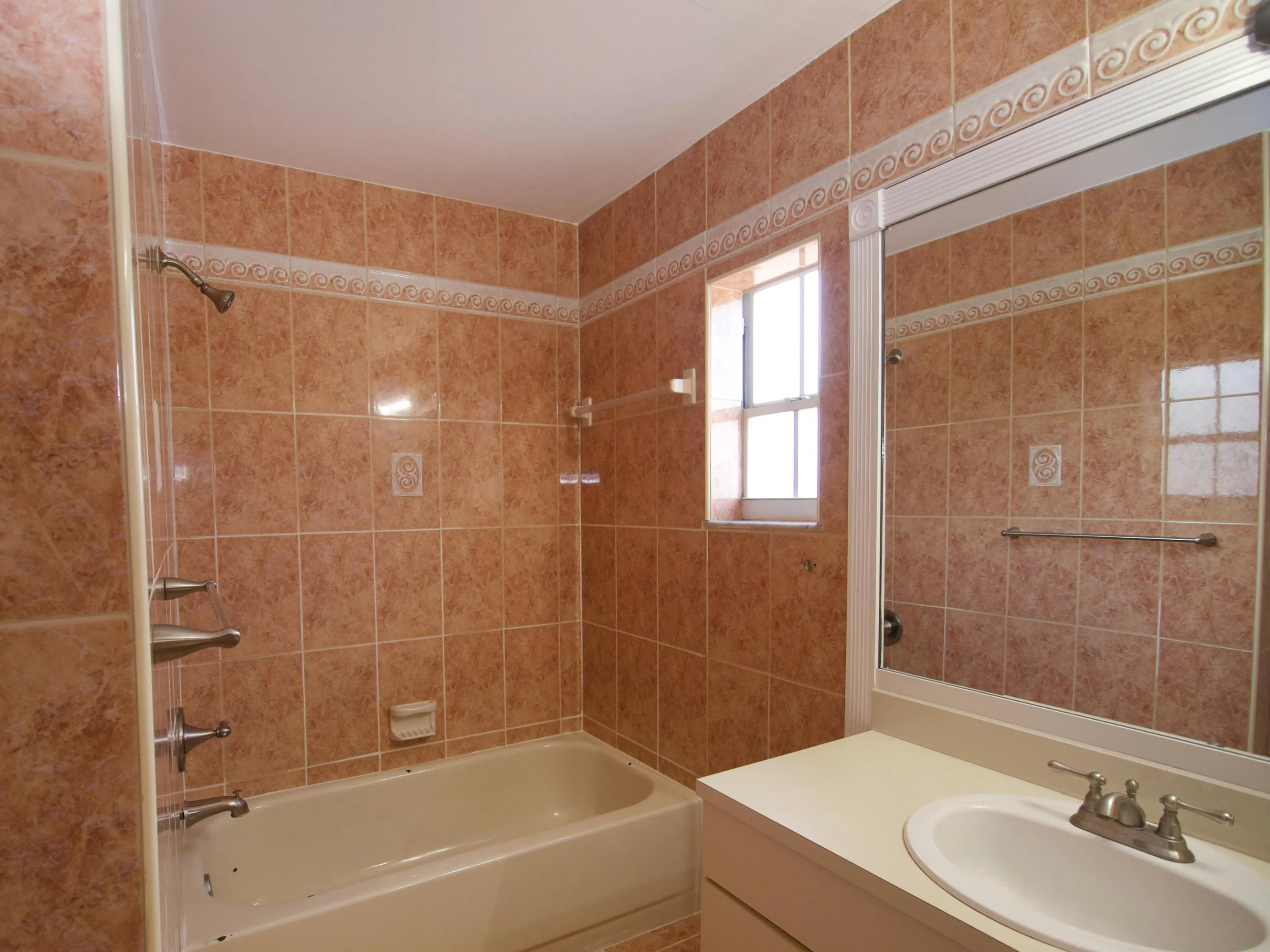 Built-in bathtub with a shower fixture, complemented by tiled walls and a decorative tile​​‌​​​​‌​​‌‌​‌‌​​​‌‌​‌​‌​‌​​​‌​​ border