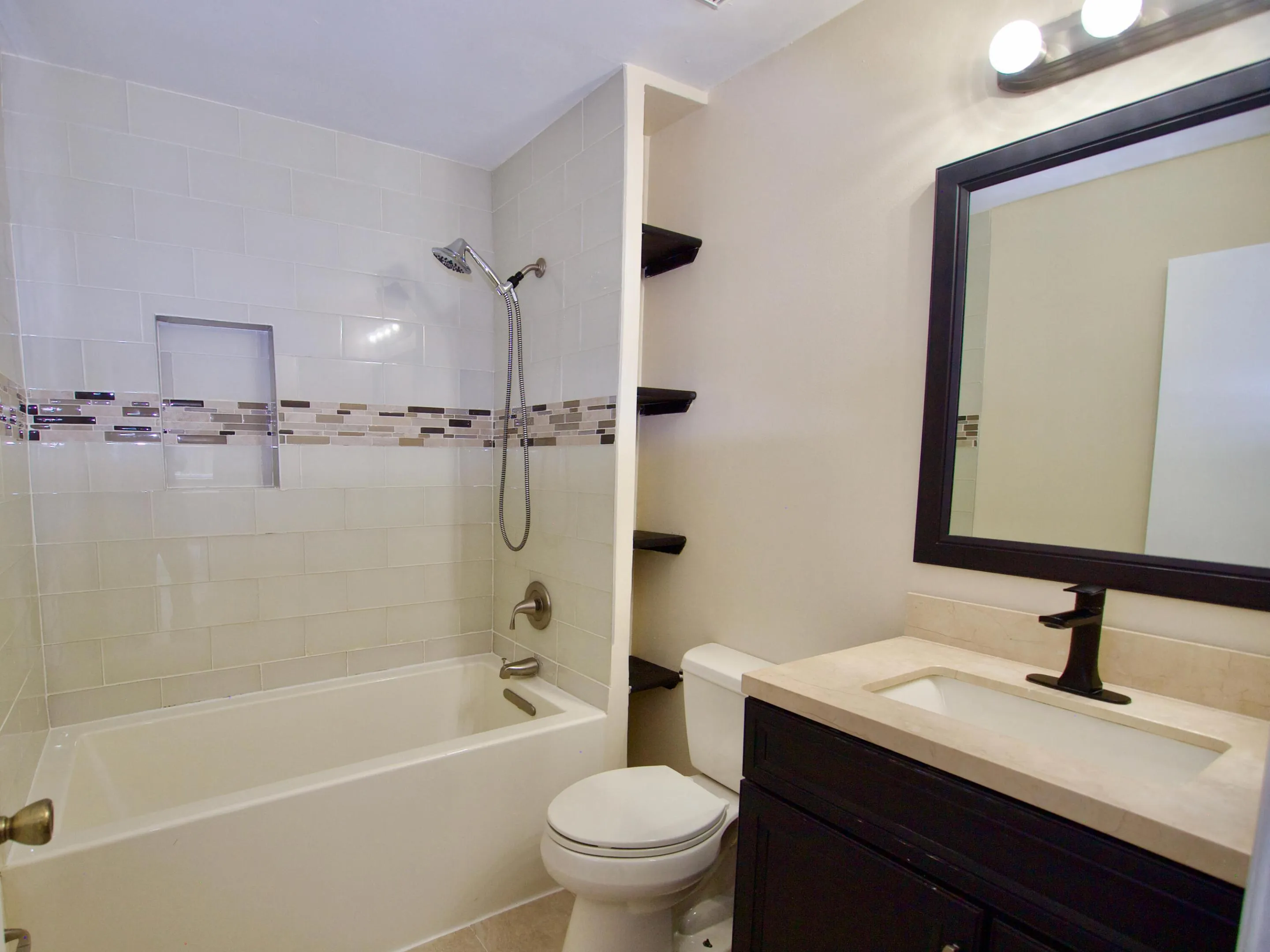 White subway tile bathtub surround with a mosaic accent band, a built-in shower niche, and a handheld showerhead