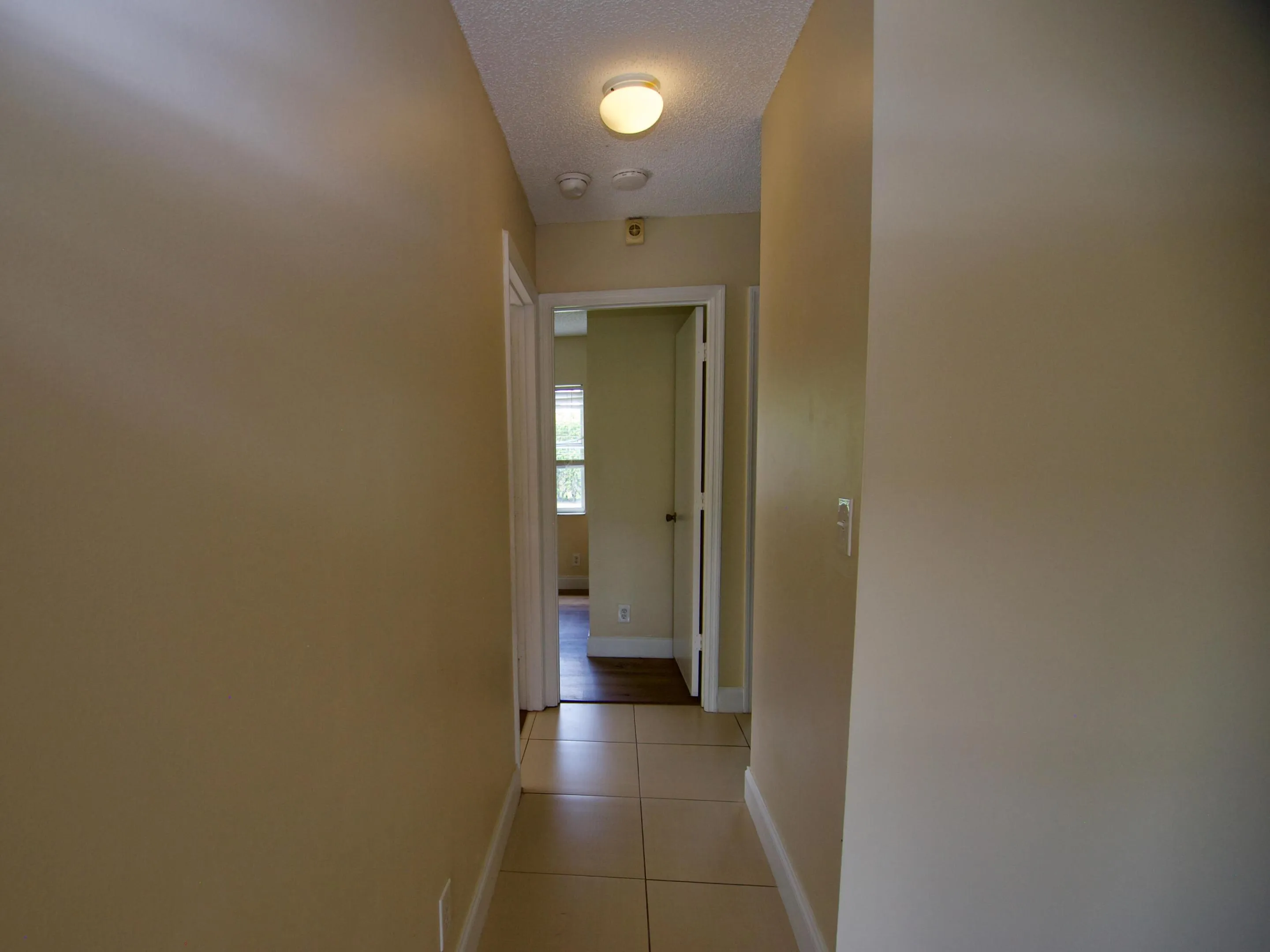 Tiled hallway flooring with a smooth ceiling, recessed lighting, and neutral wall tones