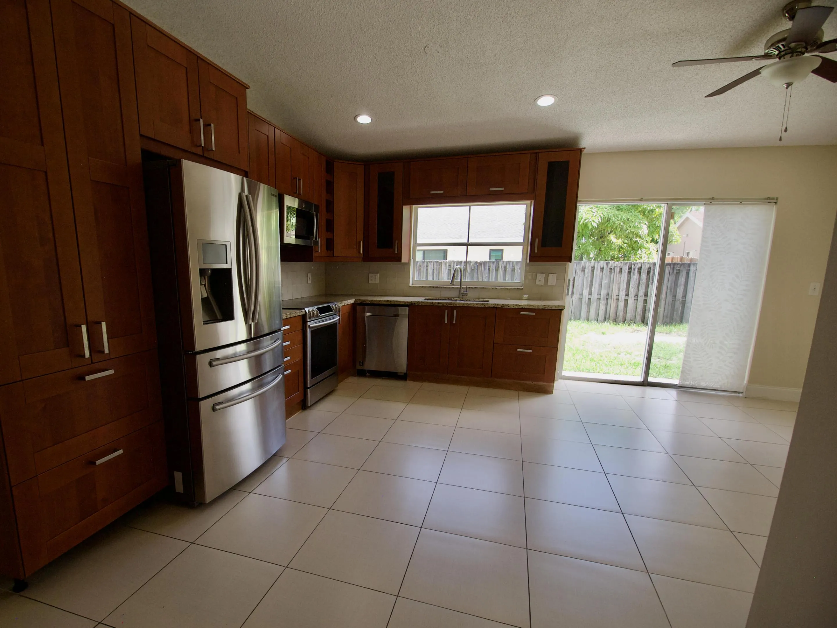 Stainless steel appliance suite, light-toned tile flooring, wood-finish cabinetry, and a sliding glass door to the backyard