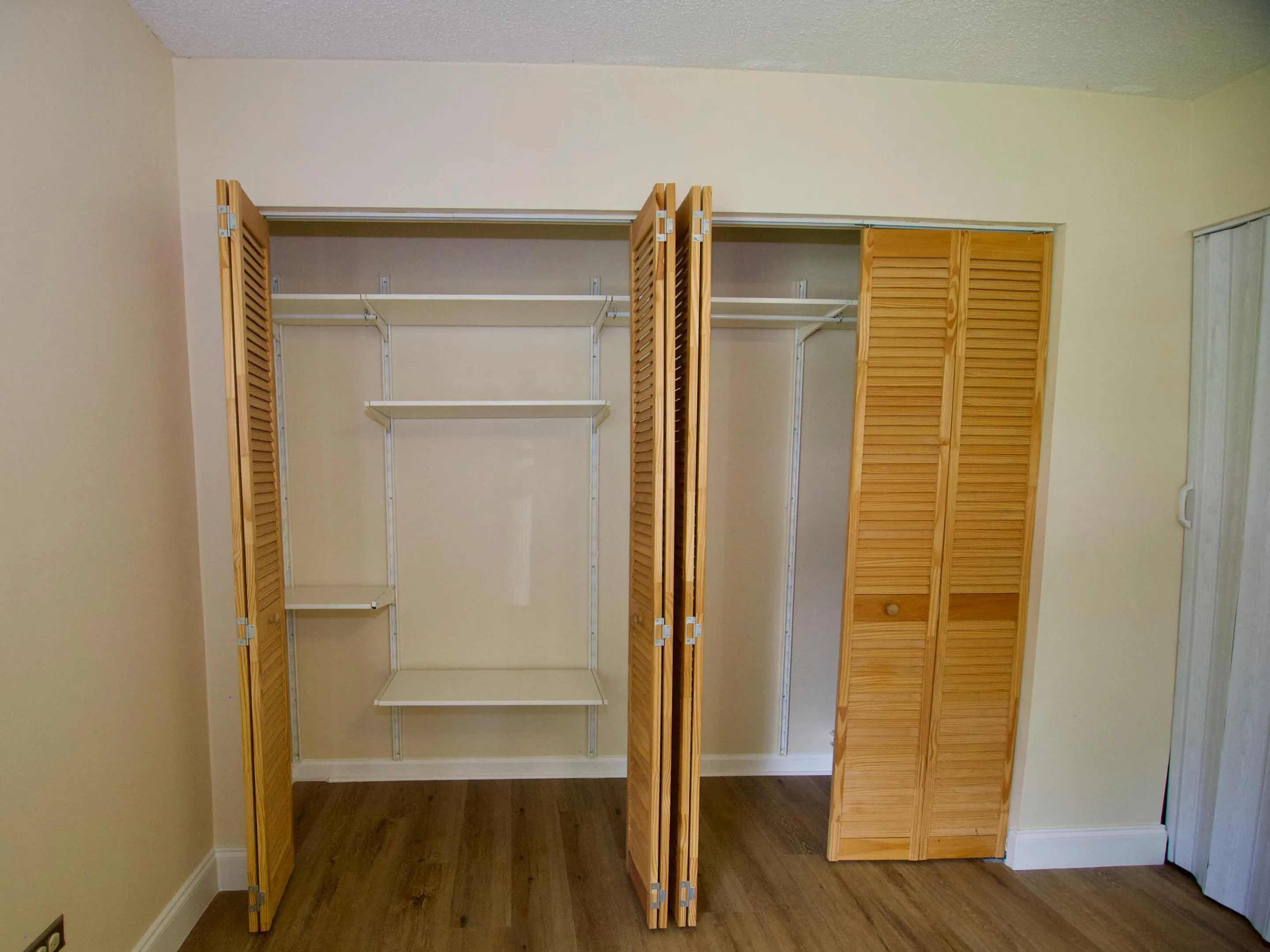 Built-in closet with louvered bi-fold doors, adjustable shelving, and wood-finish flooring