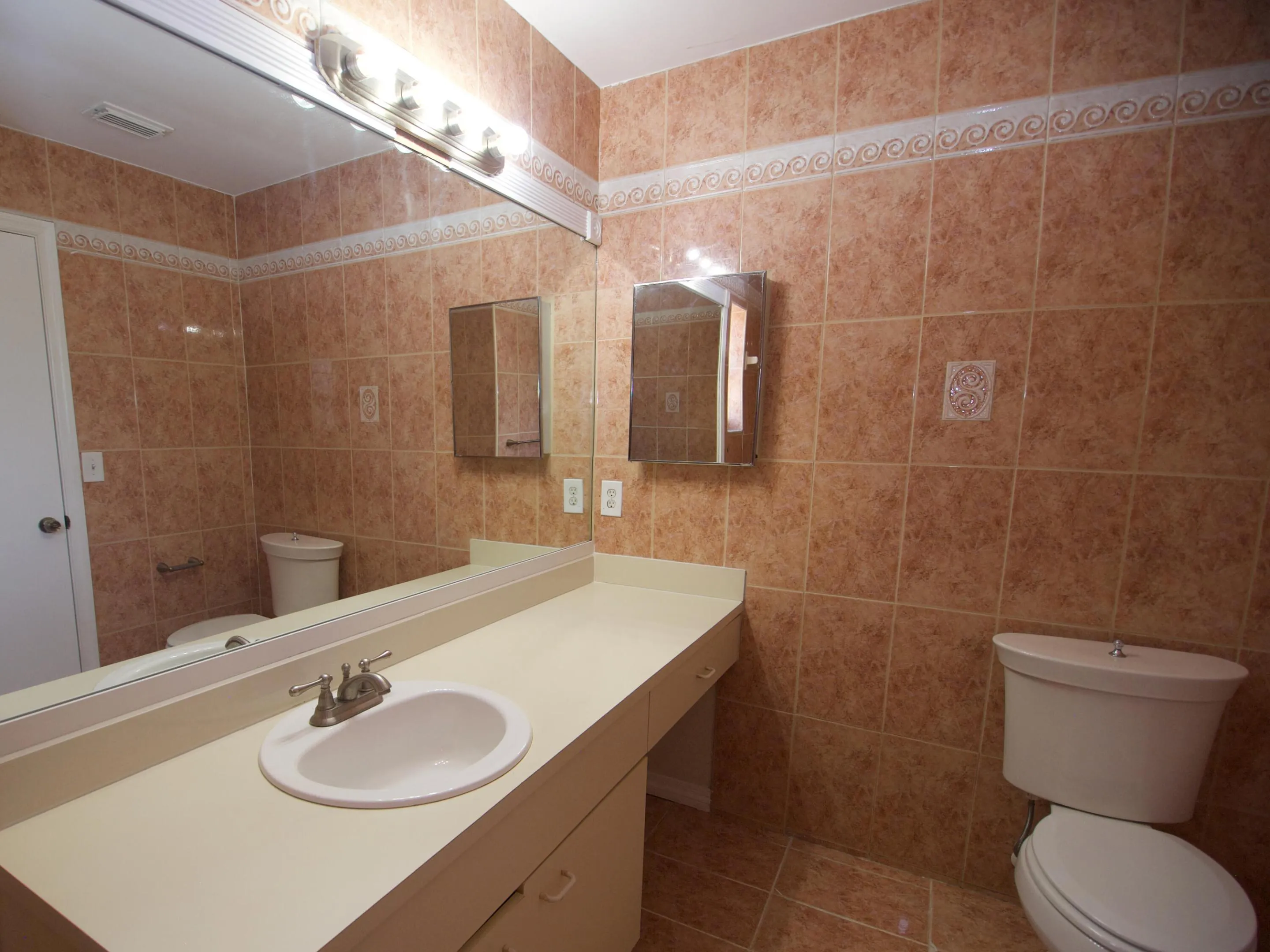 Full wall and floor tile, vanity with integrated sink, large wall-mounted mirror, medicine cabinet, and toilet