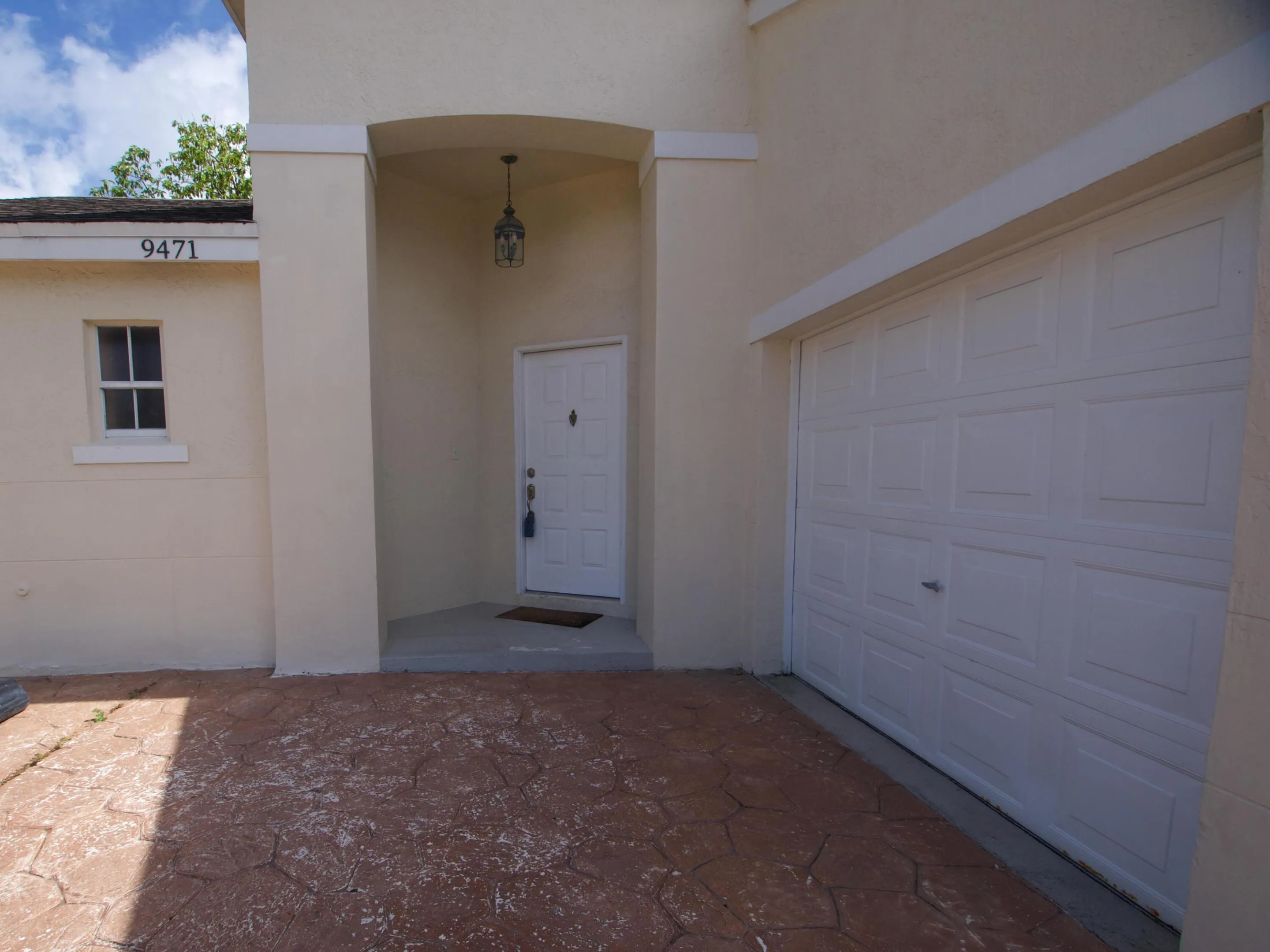 Stamped concrete driveway leading to a covered entry with an overhead fixture, paneled entry door, and an attached garage with a paneled door