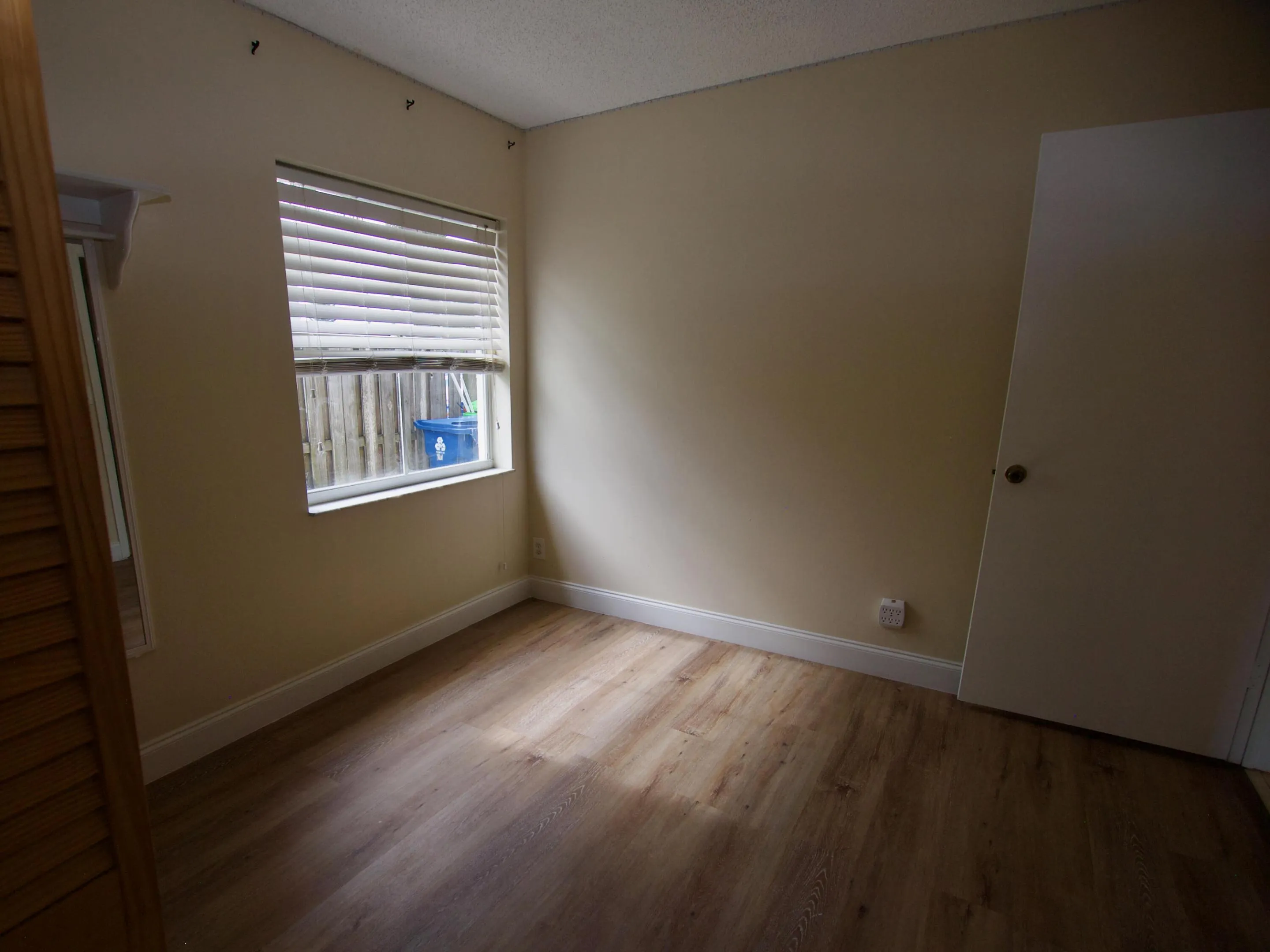 Wood-finish flooring, neutral wall paint, white trim, and a window with blinds