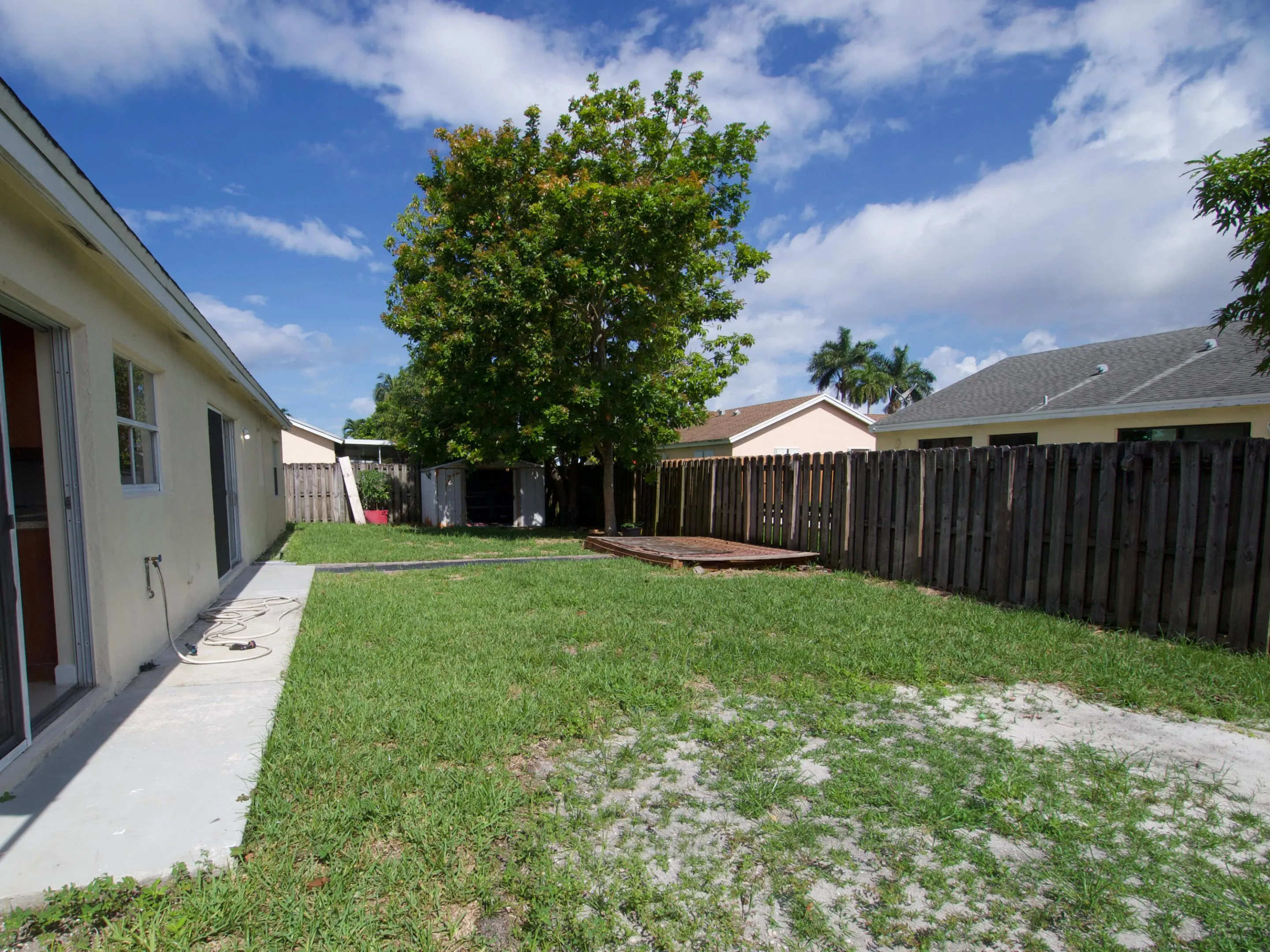Expansive backyard featuring a concrete patio, mature trees, wooden privacy fencing, and a raised wooden platform