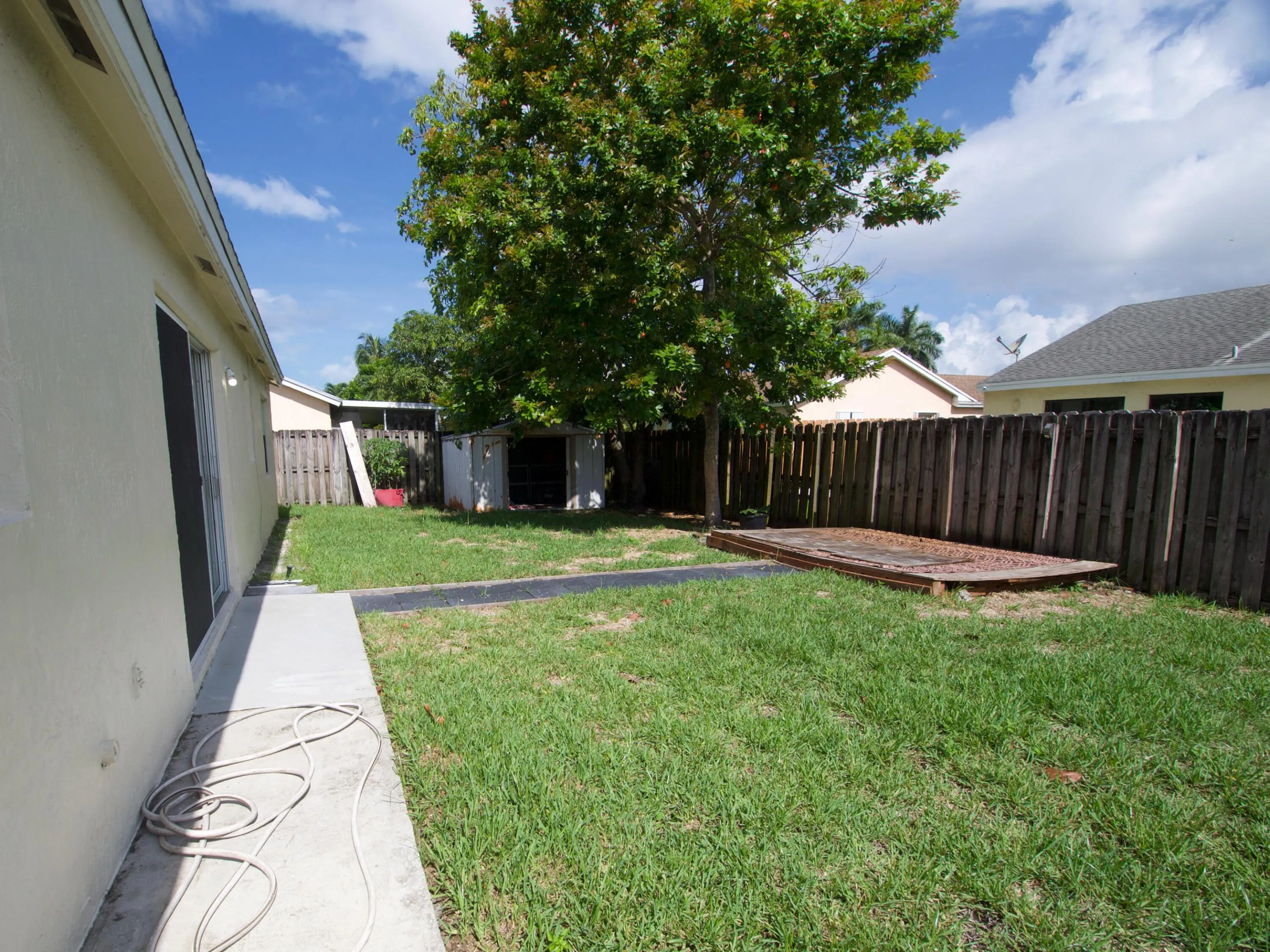 Expansive backyard featuring a concrete pathway, mature tree, wood fencing, and a utility shed