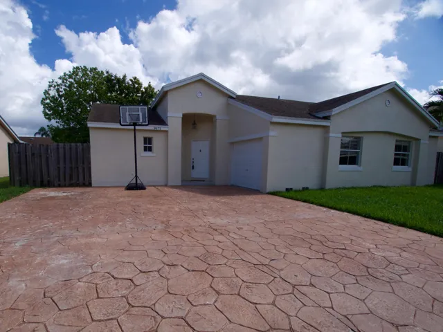 Stucco exterior featuring a prominent front entrance, attached garage, and a stamped concrete driveway