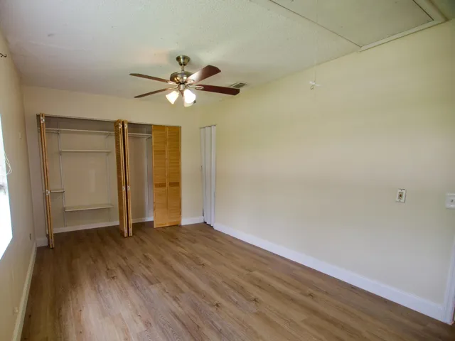 Wood-finish flooring, bi-fold closet doors, built-in closet shelving, and a ceiling fan with integrated lighting