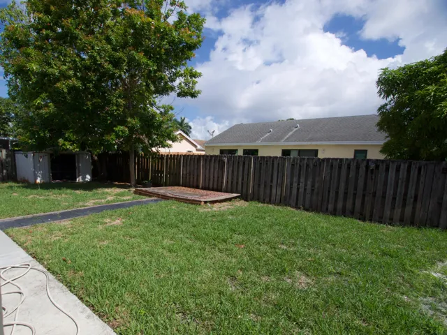 Expansive green lawn with a wooden privacy fence, mature trees, and a concrete patio area