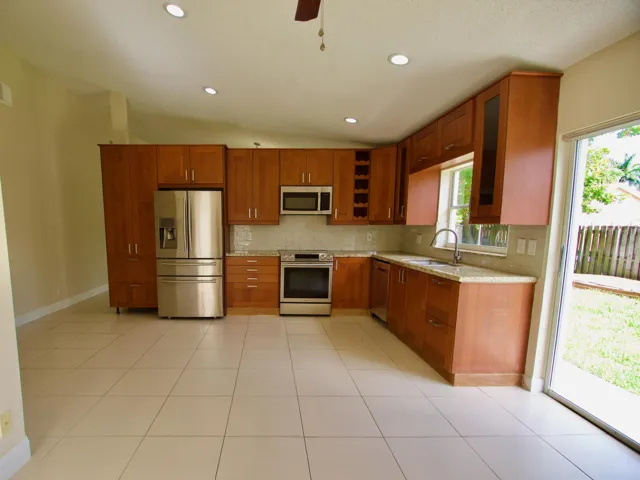 Kitchen featuring wood-finish cabinetry, stainless steel appliances, light-toned tile flooring, and recessed lighting