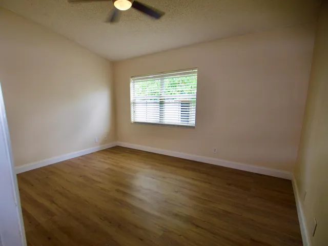 Room featuring wood-finish flooring, neutral wall tones, a ceiling fan with integrated lighting, and a single window with blinds