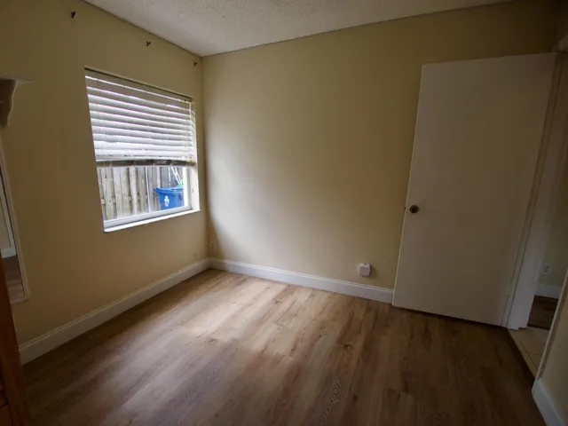 Wood-finish flooring with white trim, a single window with blinds, and neutral wall tones