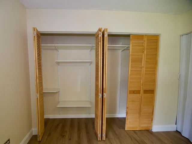 Built-in closet with louvered bi-fold doors, adjustable shelving, and wood-finish flooring