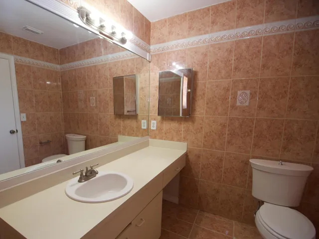 Full wall and floor tile, vanity with integrated sink, large wall-mounted mirror, medicine cabinet, and toilet
