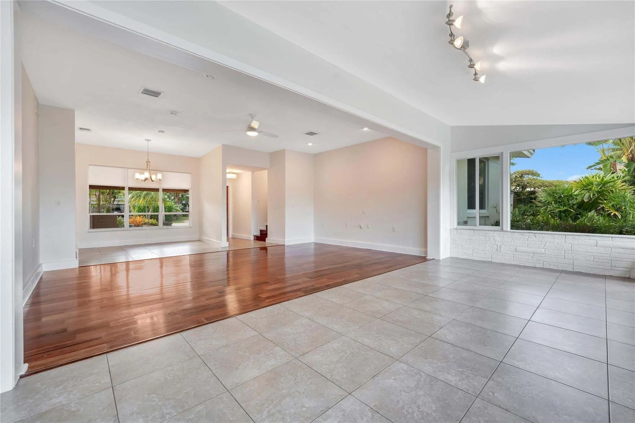 Expansive interior featuring large format tile flooring and wood-finish flooring, with a dining area illuminated by a chandelier and a sunroom with white brick paneling and track lighting