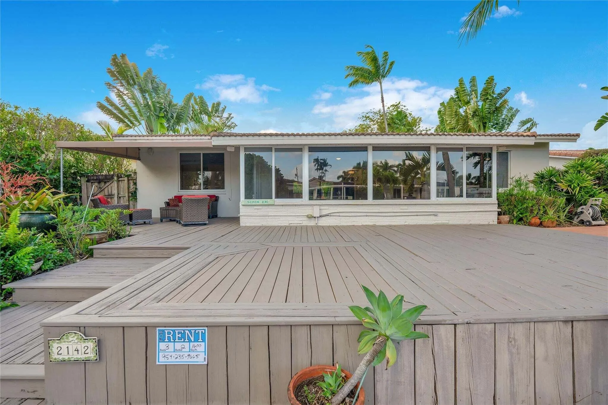 Expansive multi-level wood-finish deck with integrated steps, large windows, and a covered patio area