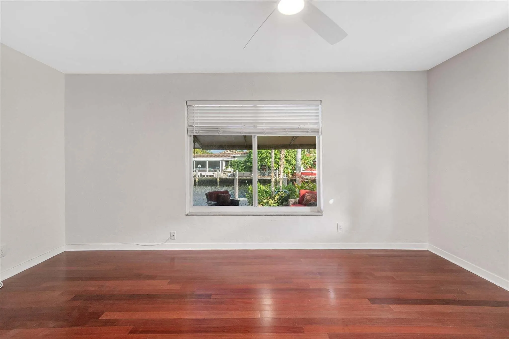 Wood-finish flooring with a window offering canal views, featuring a ceiling fan and horizontal blinds