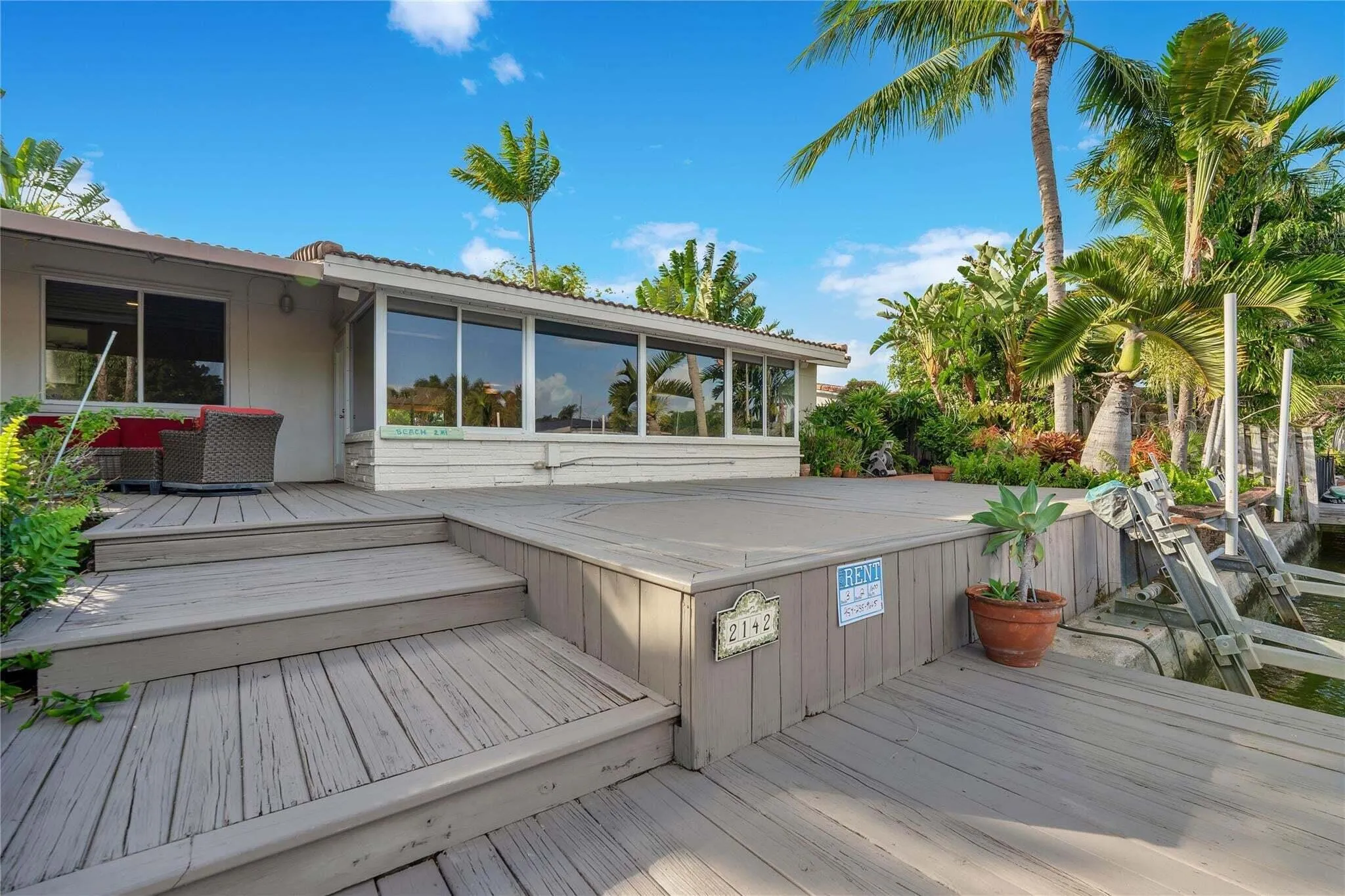 Expansive wood-finish deck with multiple levels, substantial glass panel windows, and lush tropical landscaping