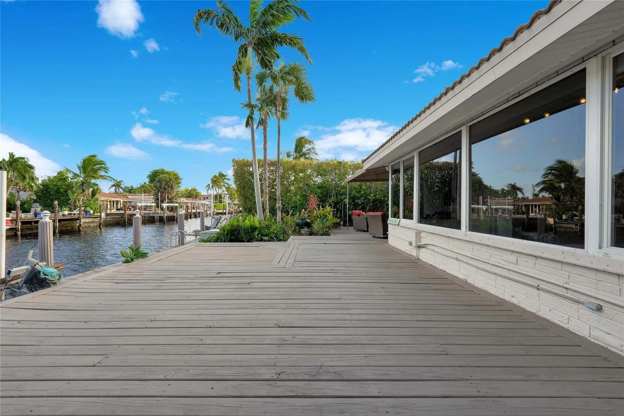 Waterfront property featuring a spacious deck, multiple dock pilings, a white brick exterior, and large picture​​‌​​​​‌​​‌‌​‌‌​​​‌‌​‌​‌​‌​​​‌​​ windows