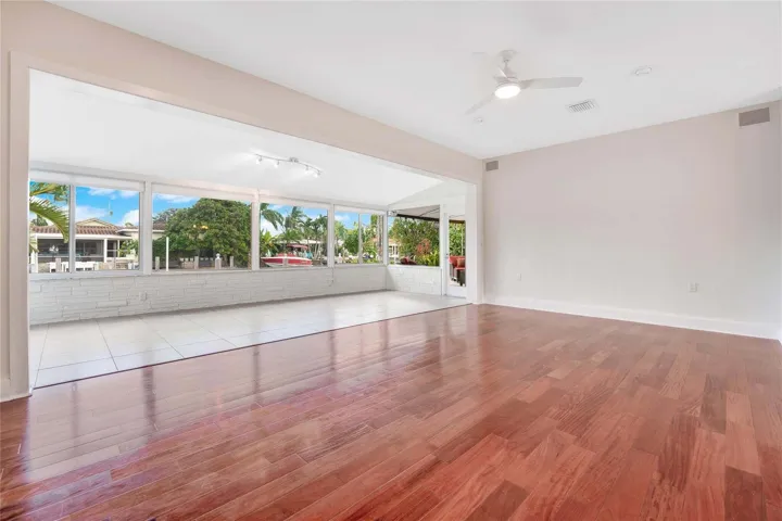 Hardwood flooring in the main room, with an expansive opening to a sunroom featuring large windows, white tile flooring, and track lighting