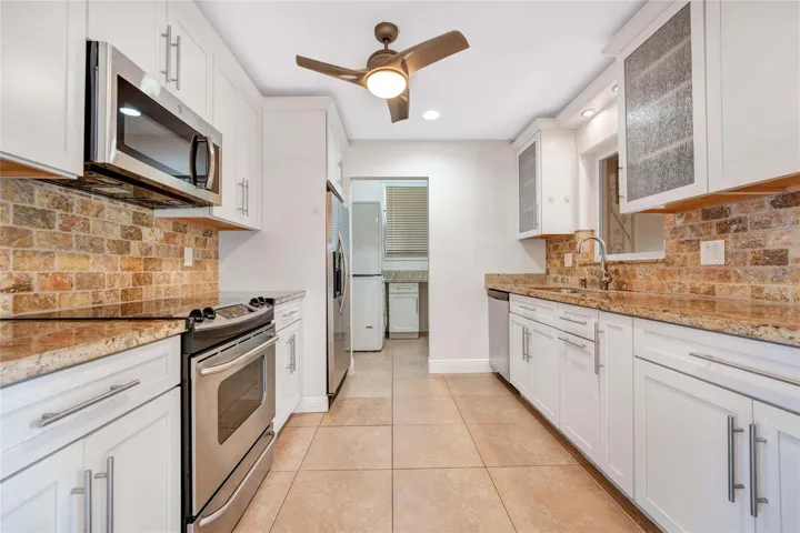 Kitchen featuring white cabinetry, stone tile backsplash, stainless steel appliances, granite countertops, and ceiling fan with integrated lighting