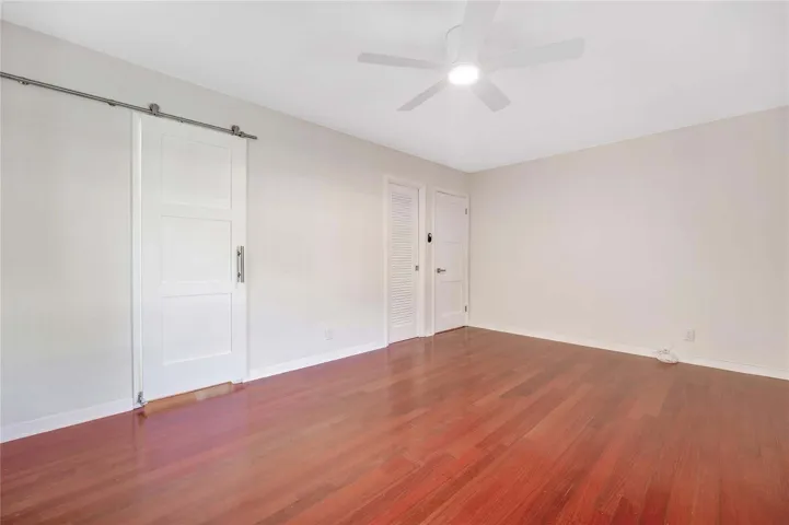 Rich wood-finish flooring, white walls, and a ceiling fan with integrated lighting