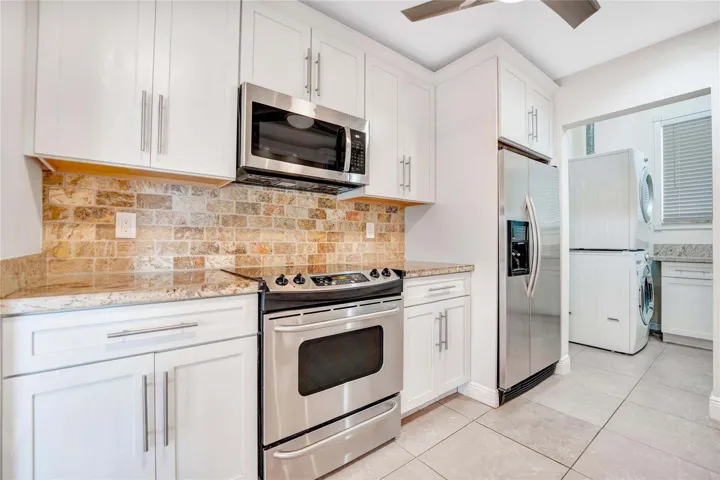 White cabinetry with brushed nickel pulls, stainless steel appliances, tile flooring, and a mosaic tile backsplash