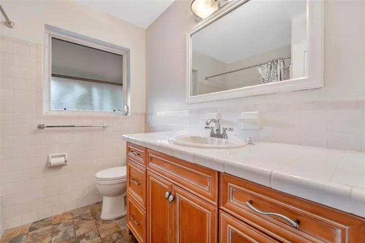 Wood-finish vanity with an integrated sink, ceramic tile countertop, and chrome fixtures