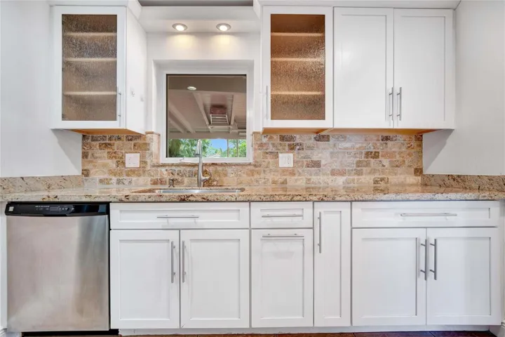 White shaker-style cabinetry with stainless steel hardware, granite countertops, and a brick-patterned tile backsplash