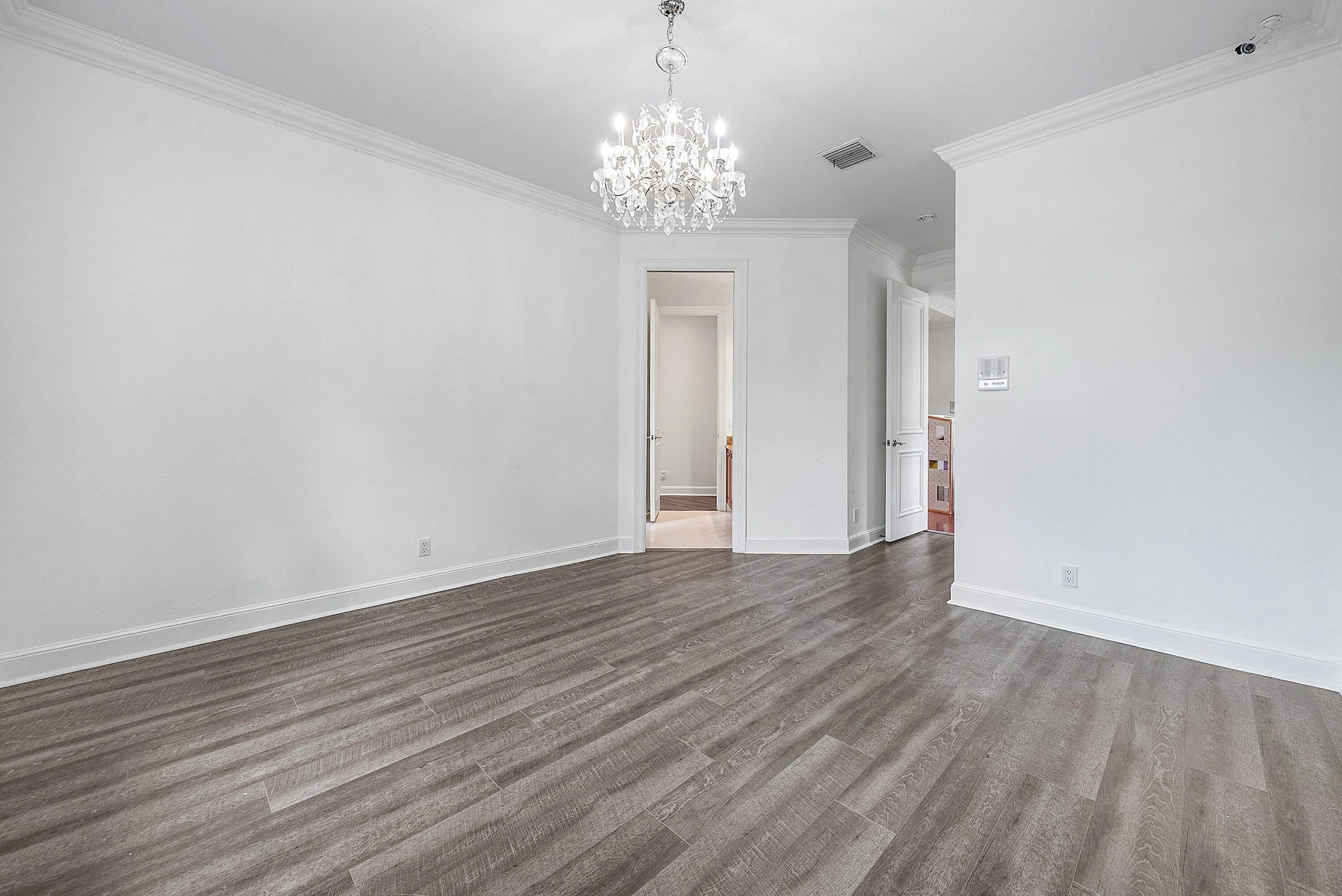 Wood-finish flooring, crown molding, white paneled doors leading to shared bathroom