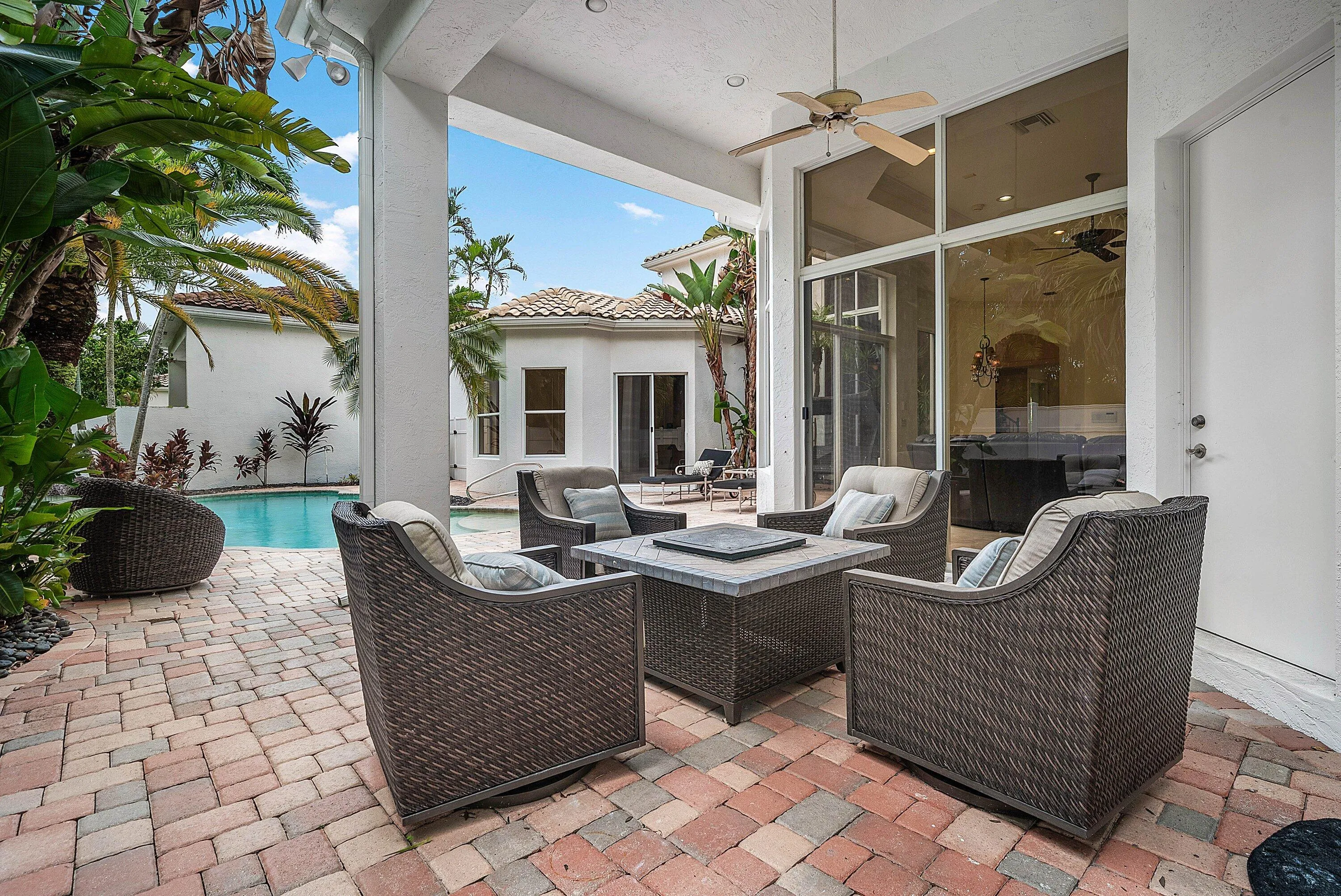 Covered outdoor patio with a ceiling fan, paver flooring, expansive glass sliding doors