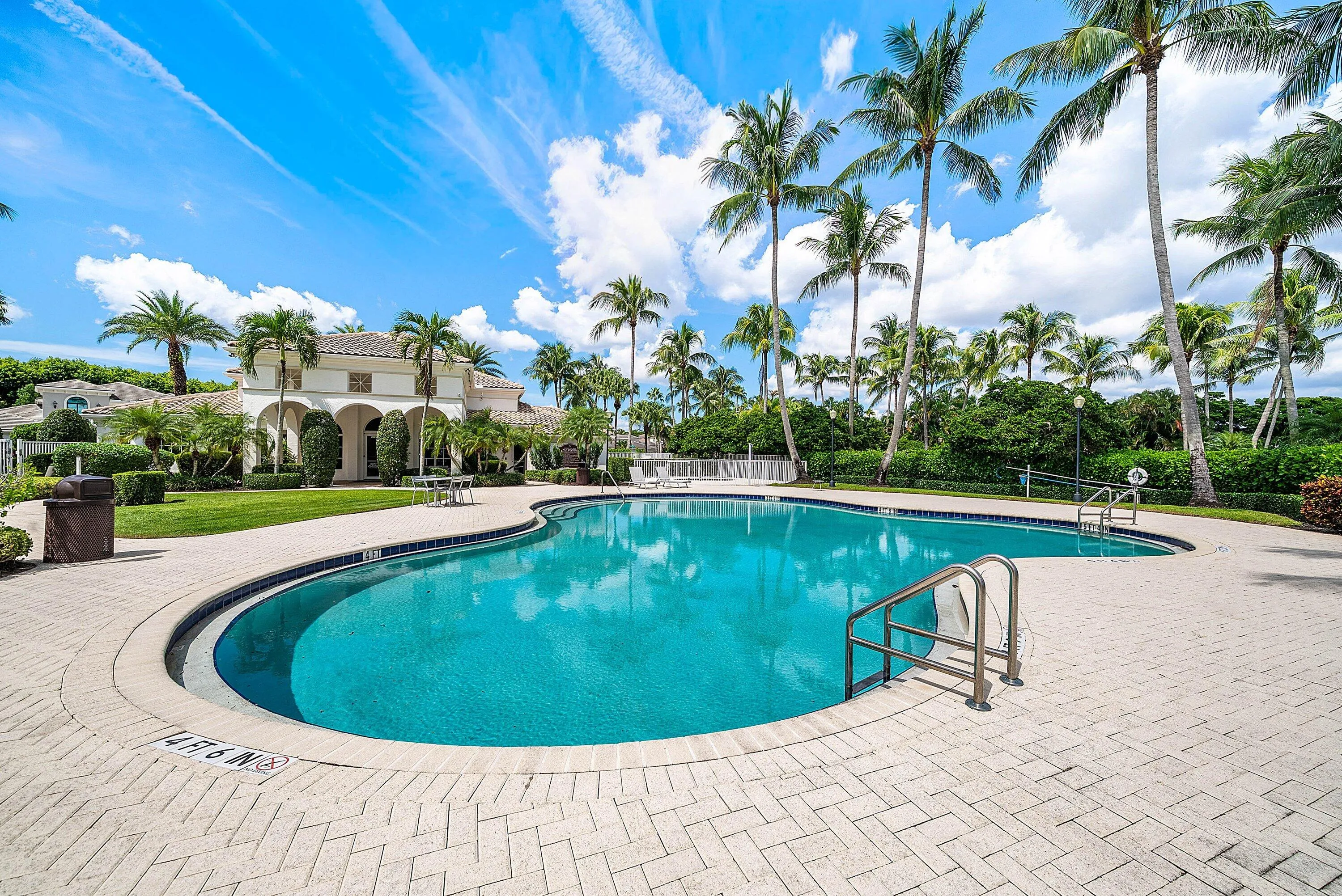 Freeform swimming pool with brick paver decking, surrounded by mature palm trees and lush landscaping
