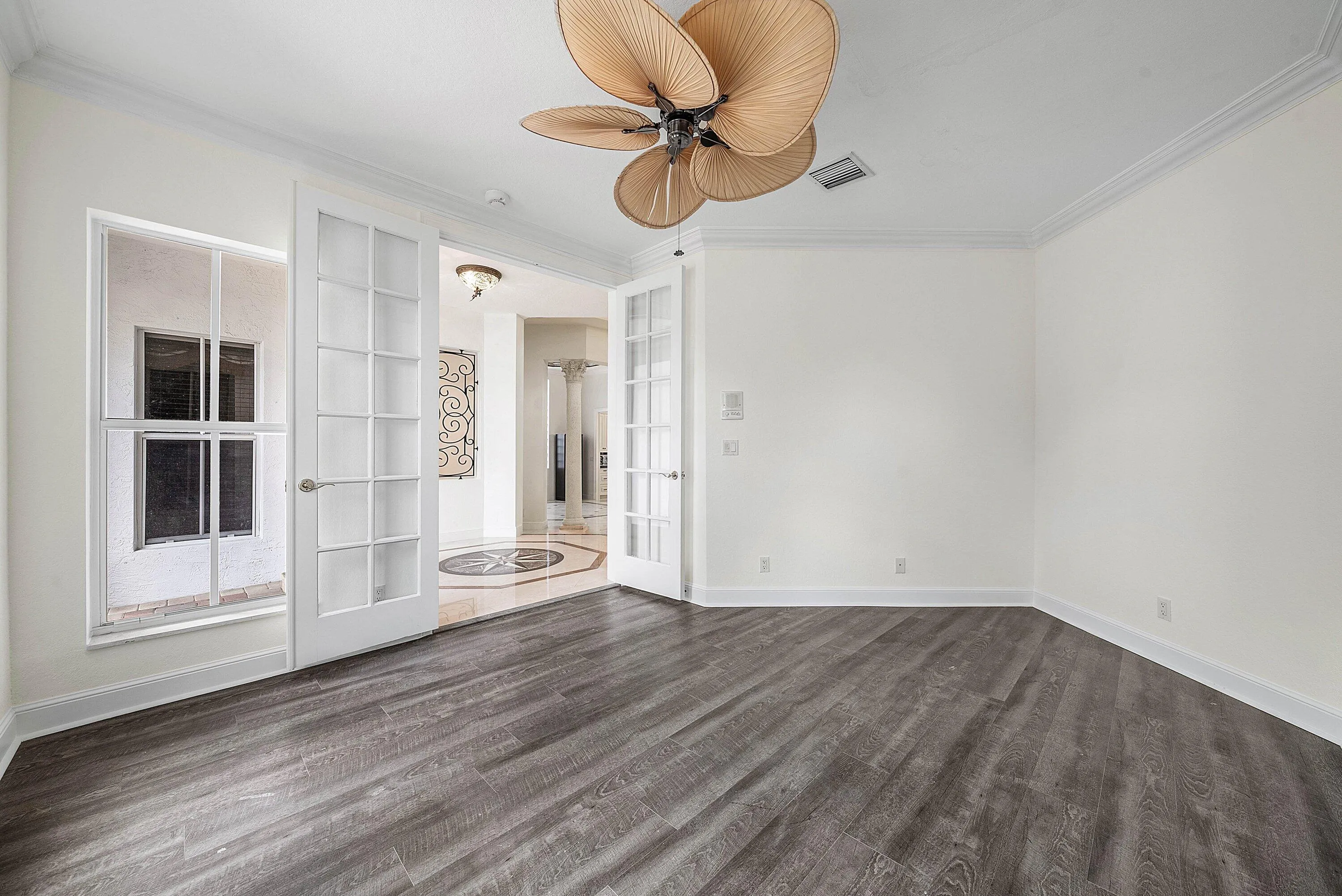 Wood-finish flooring, crown molding, double French doors, large window, and ceiling fan