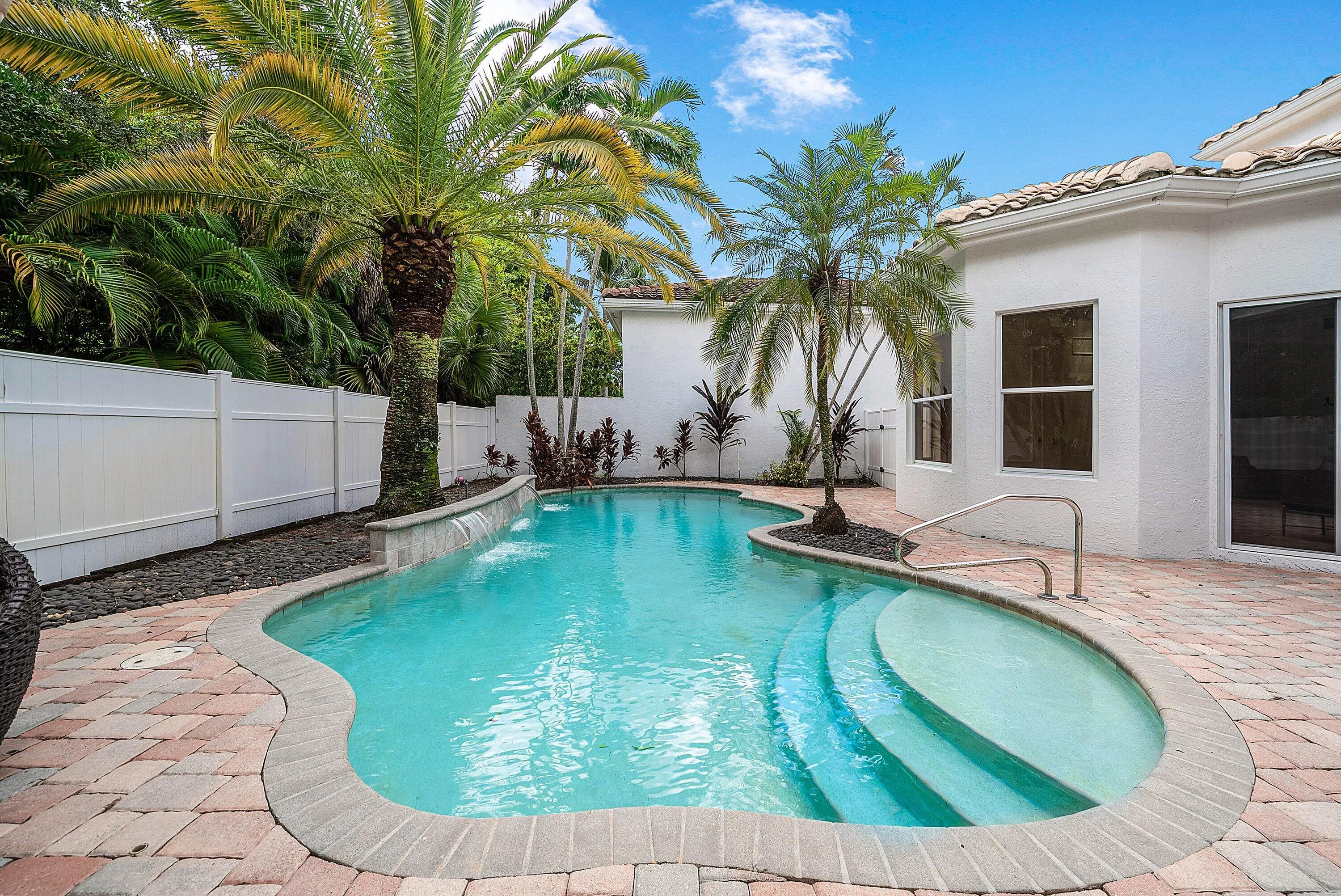 Freeform swimming pool with a stone coping, integrated waterfall feature, and built-in steps