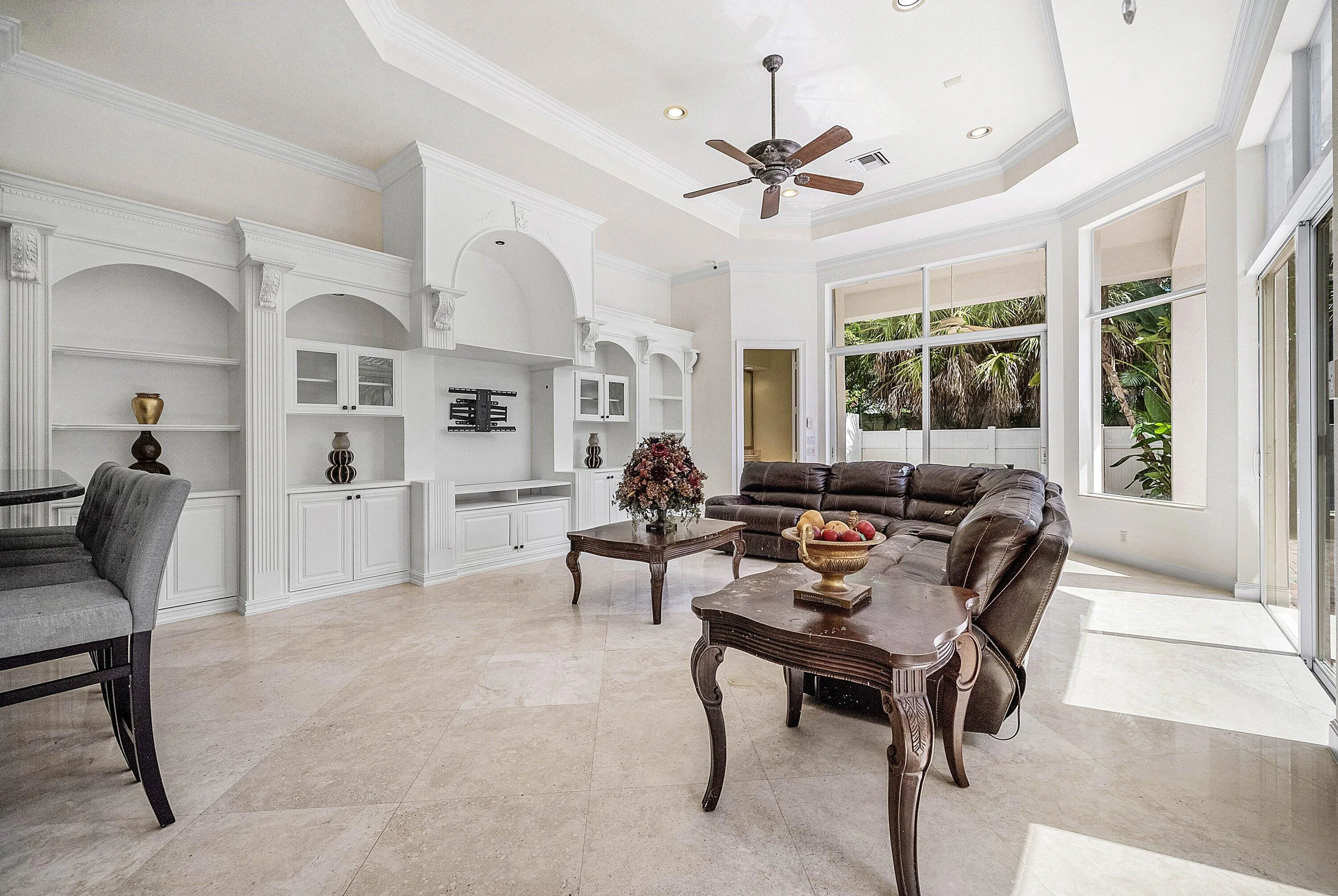 Built-in white cabinetry with arched details, tray ceiling with recessed lighting, ceiling fan, large windows, and marble flooring