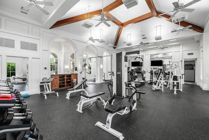 High vaulted ceiling with exposed wood beams, multiple ceiling fans, wide range of fitness equipment