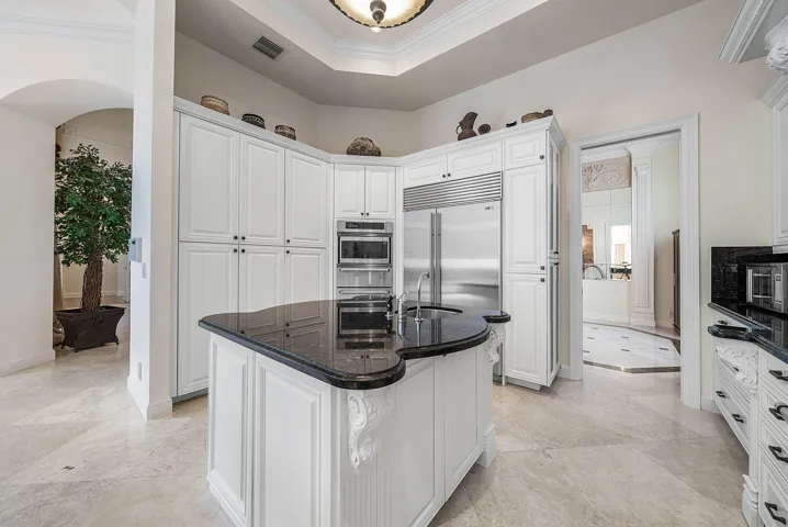 White paneled cabinetry, curved granite island with integrated sink, Sub Zero fridge, Thermador wall oven.