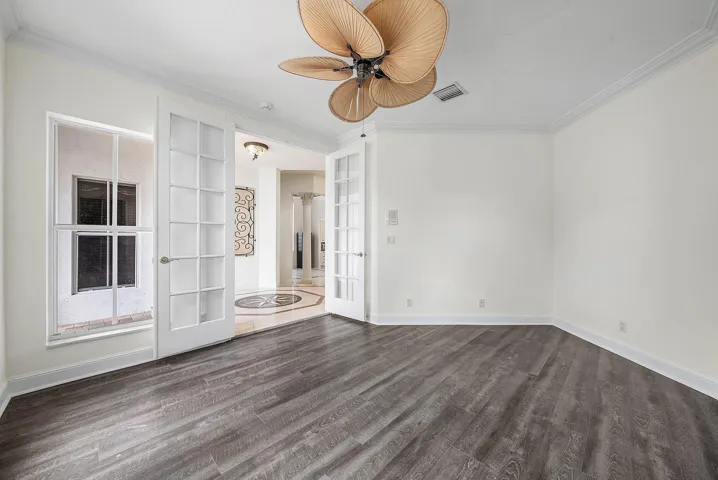 Wood-finish flooring, crown molding, double French doors, large window, and ceiling fan