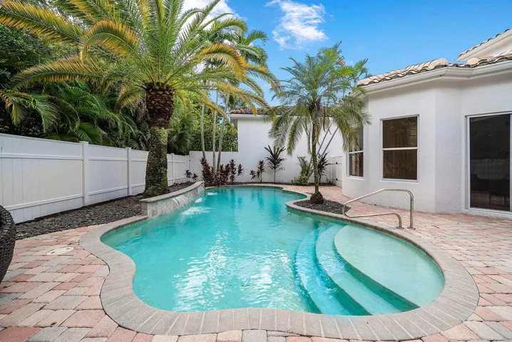Freeform swimming pool with a stone coping, integrated waterfall feature, and built-in steps