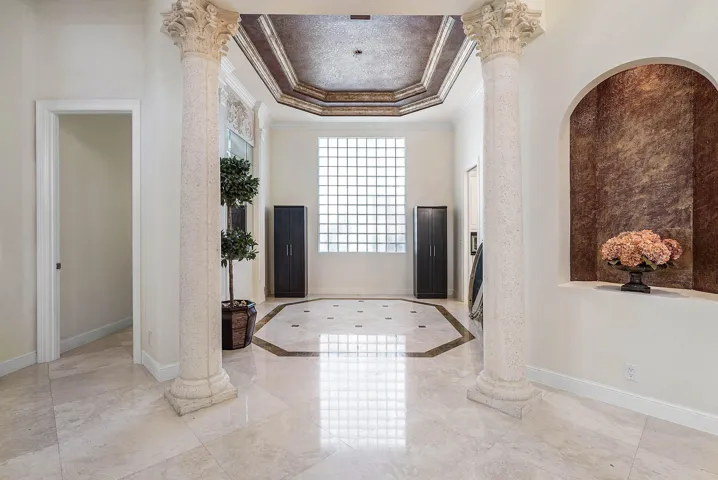 Polished marble flooring with an inlaid geometric pattern, decorative columns, a coffered ceiling, an arched wall niche, and a glass block window