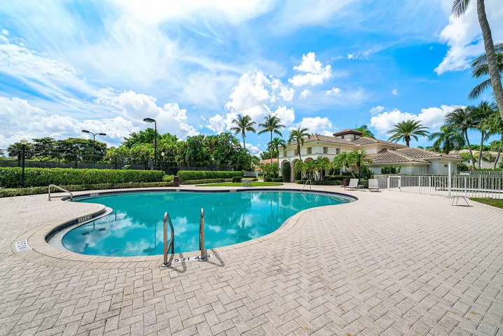 Curved swimming pool with a paver deck, surrounded by manicured landscaping and palm trees