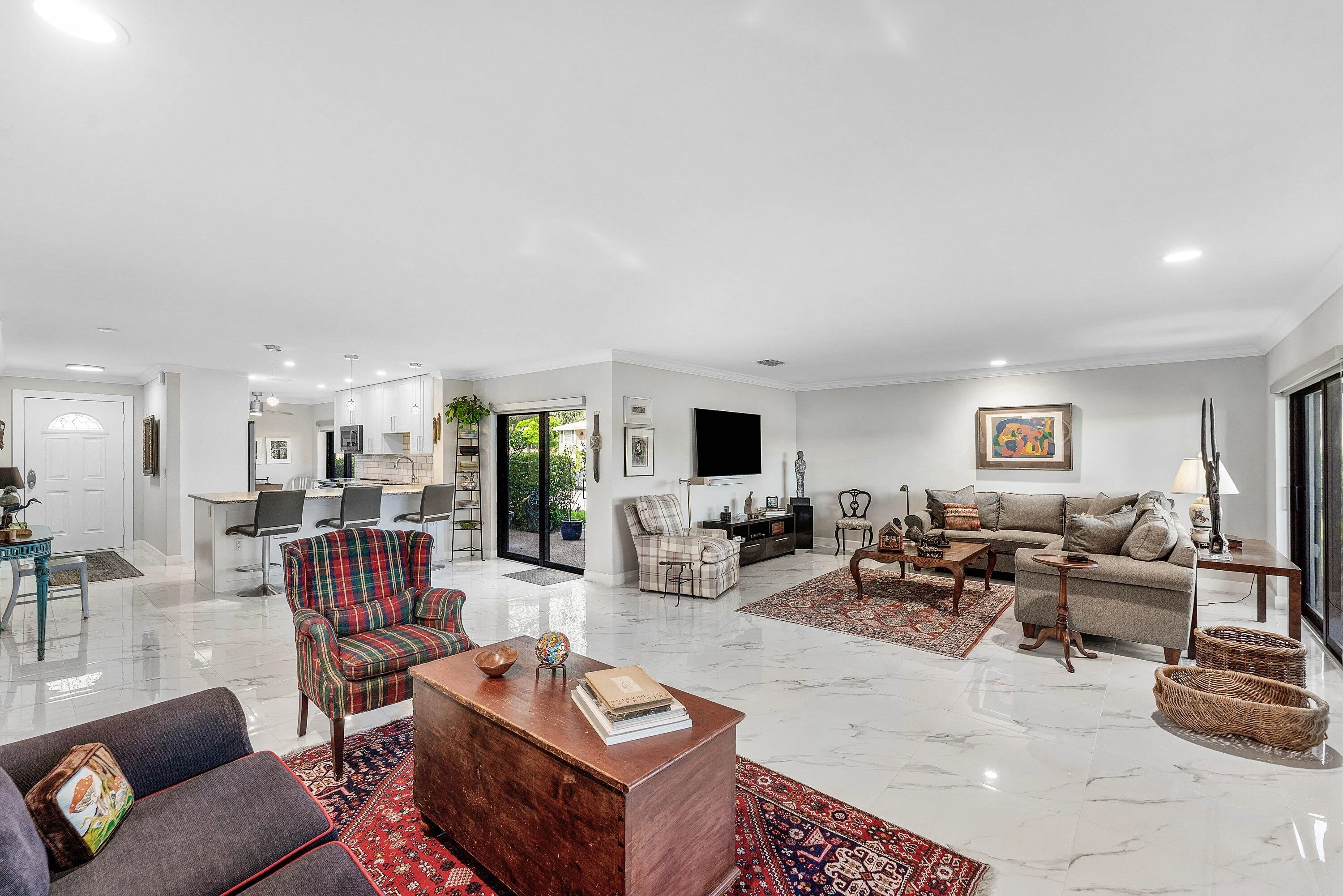 Spacious open-concept living area featuring polished tile flooring, recessed lighting, crown molding, and a sliding glass door