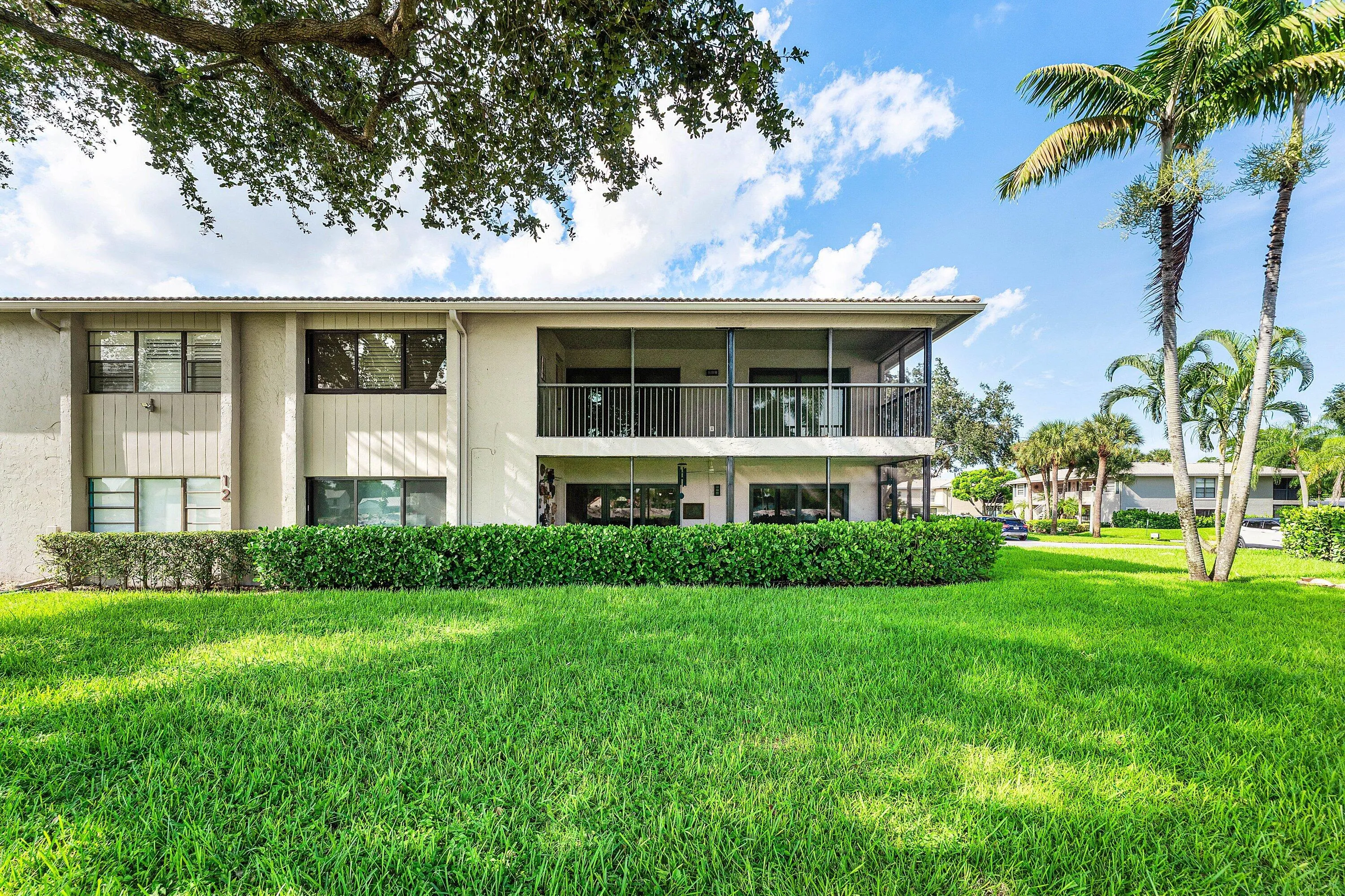 Exterior building featuring multiple screened balconies and patios, surrounded by mature landscaping and a well-maintained lawn