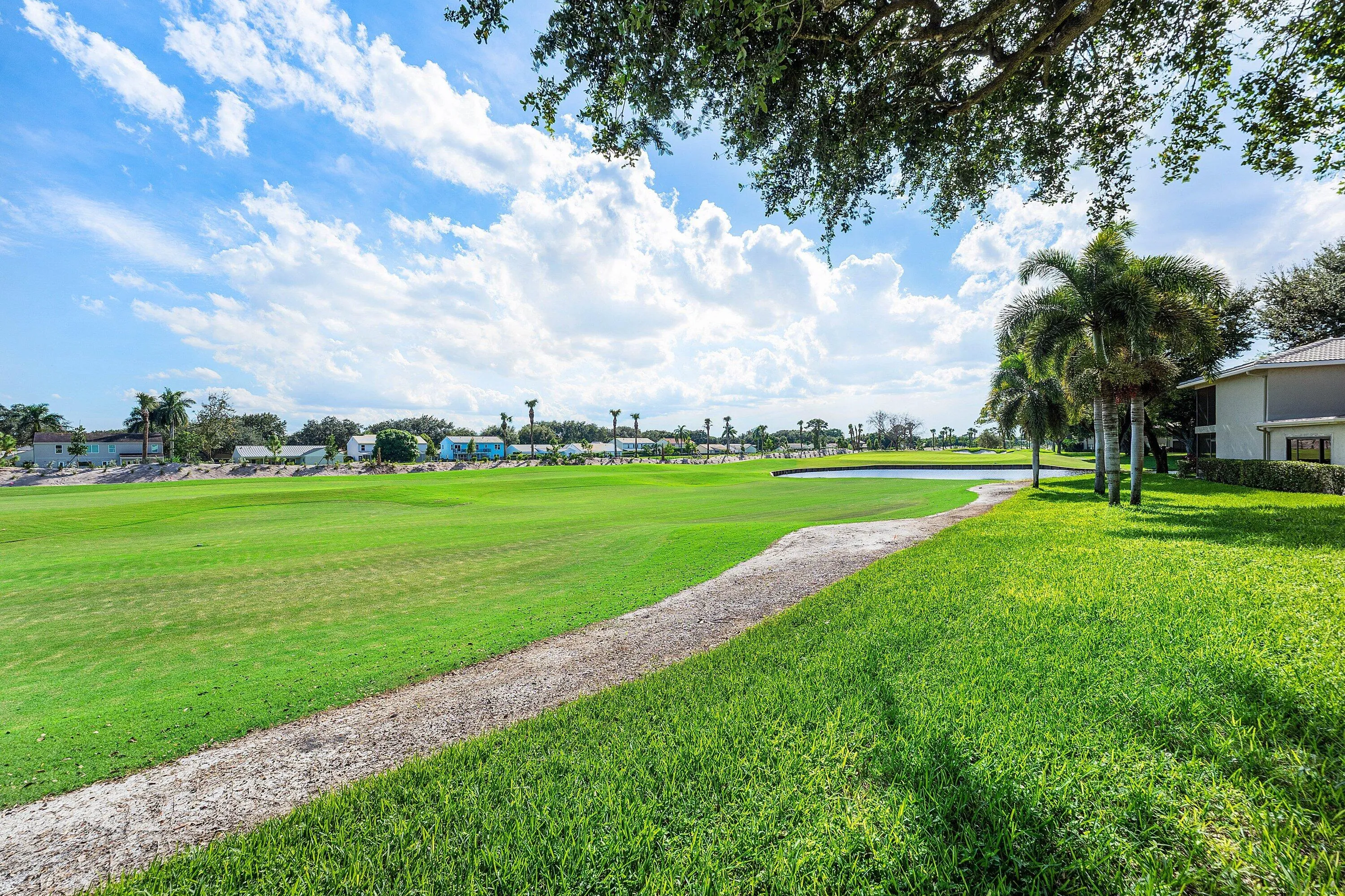 Expansive green space featuring a water element, mature palm trees, and a visible building structure
